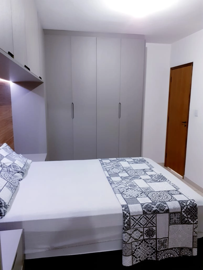 Quarto organizado com cama de colcha estampada, guarda-roupa e prateleiras